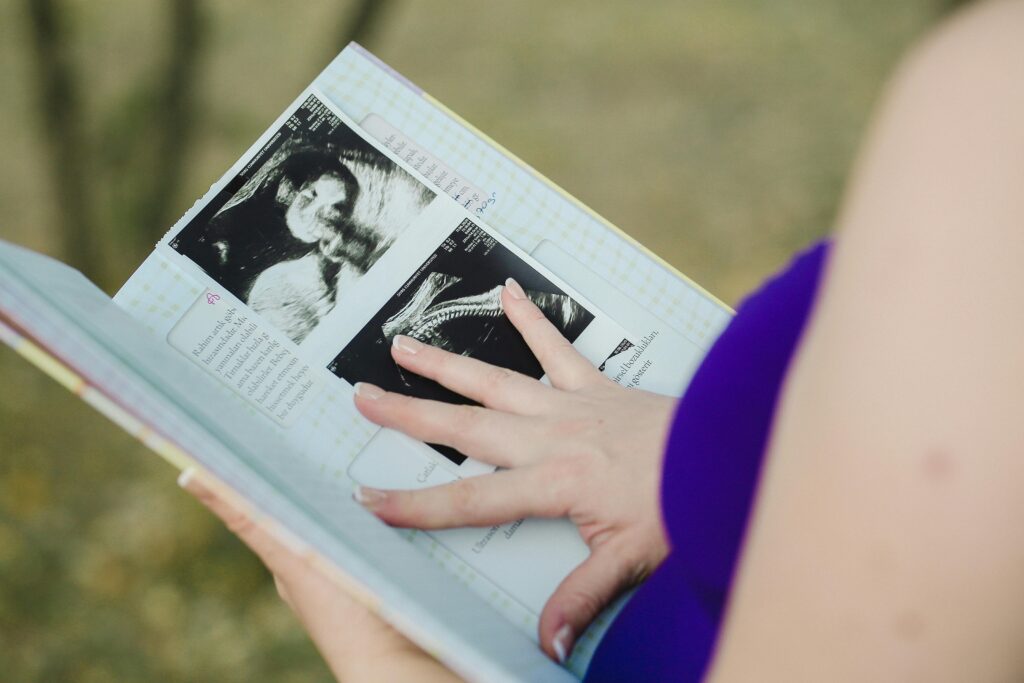 A woman gently touches ultrasound images in an open notebook, highlighting prenatal memories.